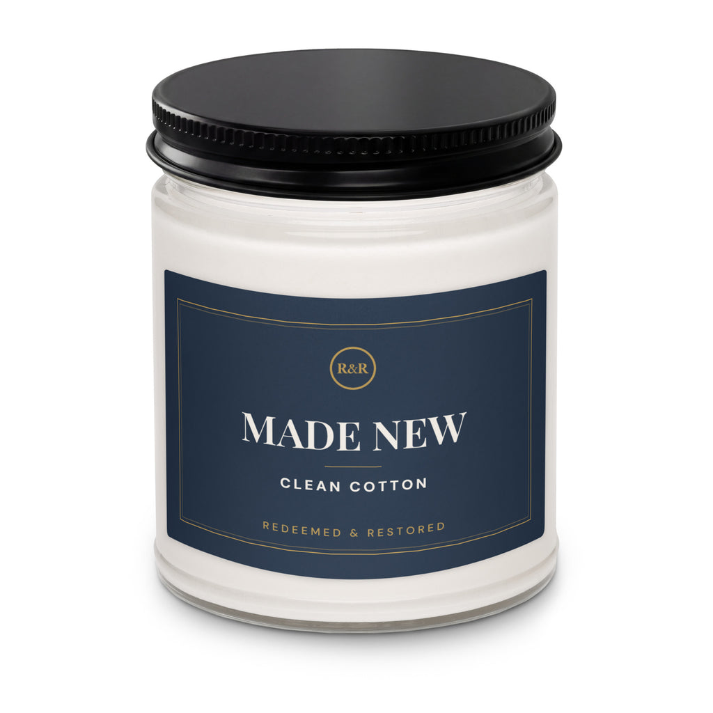 Close-up of the Made New candle jar with black lid, showing the navy label with gold border and Clean Cotton scent name