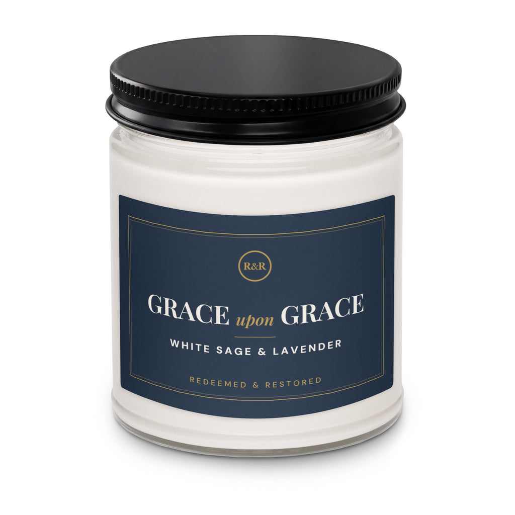 Close-up of the Grace Upon Grace candle jar with black lid, showing the navy label with gold border and White Sage & Lavender scent name